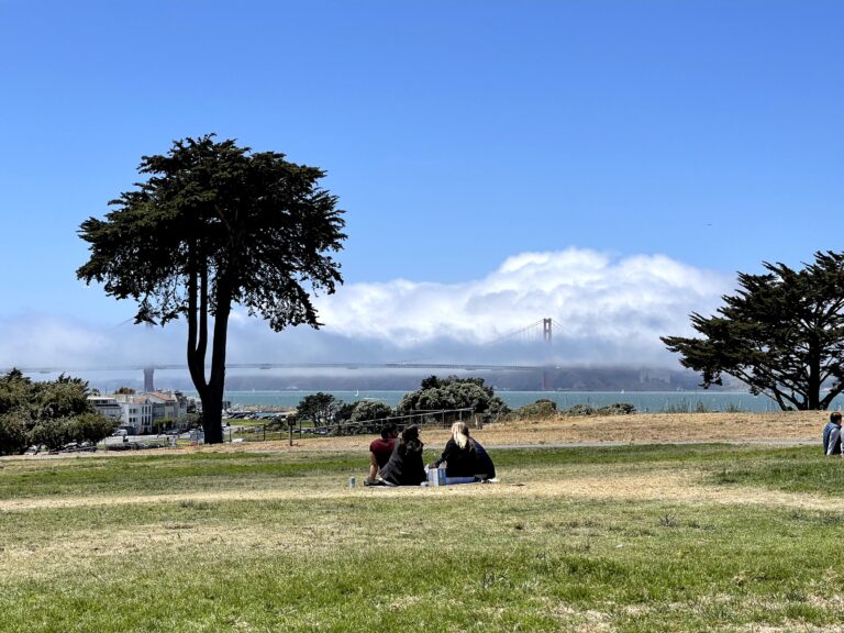 Golden Gate Bridge shrouded in fog viewed from a San Francisco park with friends picnicking on the grass